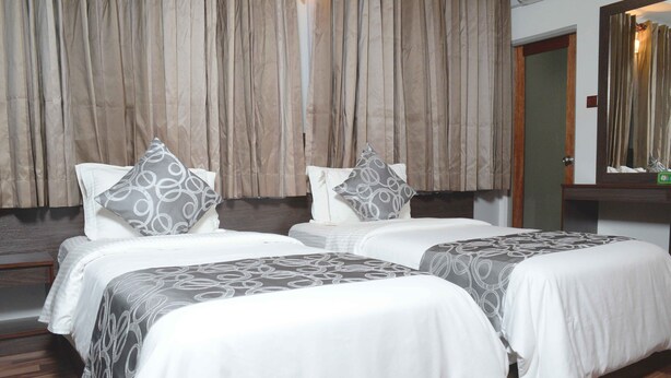 A hotel room with two beds, each with a patterned bedspread and pillows, a wooden floor, and a large mirror on the wall.