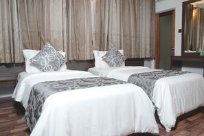 A hotel room with two beds, each with a patterned bedspread and pillows, a wooden floor, and a large mirror on the wall. - North Edge Inn (Kanditheemu)
