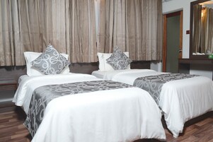 Quarto de hotel com duas camas, cada uma com colcha e almofadas estampadas, piso de madeira e um espelho grande na parede.