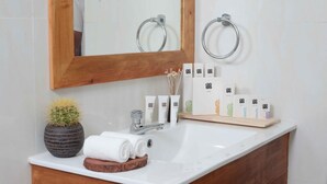 A bathroom with a wooden vanity, a sink, a mirror, and toiletries.