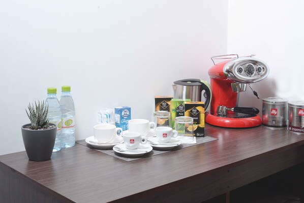 A coffee station with a red coffee maker, cups, saucers, and various coffee pods. - North Edge Inn (Kanditheemu)