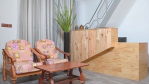 A room with two patterned armchairs, a wooden coffee table, a wooden cabinet, and a potted plant.