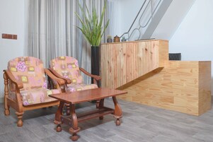 Um quarto com duas poltronas estampadas, uma mesa de centro de madeira, um armário de madeira e um vaso de planta.
