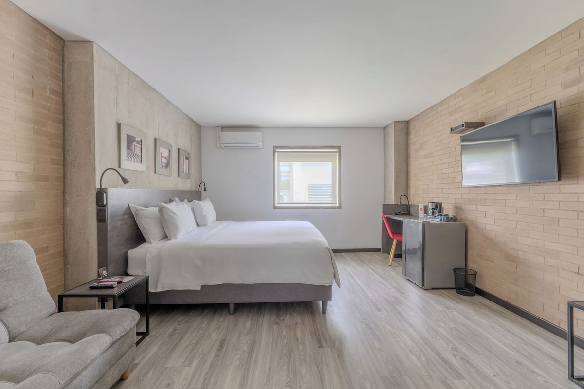 A modern hotel room with a bed, a desk, a TV, and a window.