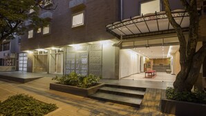 A modern hotel entrance with a glass facade, outdoor seating, and a landscaped area with plants. - Hotel Quinta Norte Chipichape Cali (Cali)