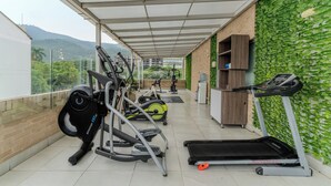 A covered outdoor gym area with exercise equipment, a treadmill, and a view of a hilly landscape. - Hotel Quinta Norte Chipichape Cali (Cali)