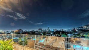 A rooftop terrace with a glass railing, a sofa, and a view of a cityscape at night. - Hotel Quinta Norte Chipichape Cali (Cali)