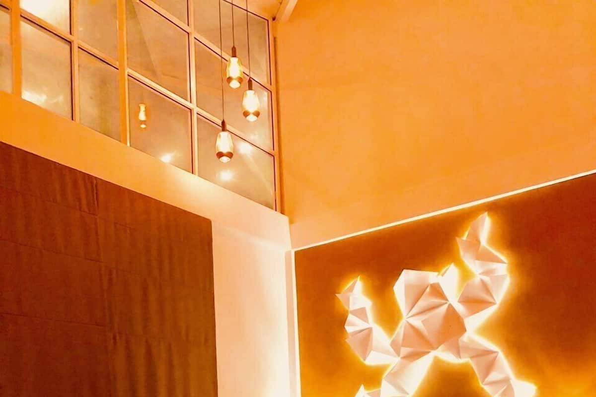 Habitación de hotel moderna con una cama, una mesa redonda y una lámpara de pared con un diseño geométrico único.