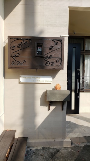 A wooden plaque with a name and address, a small piggy bank, and a door with a window. - Turquoise Mihama (Chatan)