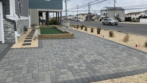 A paved driveway leading to a house with a front porch and a small garden area.