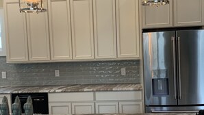A kitchen with light-colored cabinets, a stainless steel refrigerator, a marble countertop, and a built-in dishwasher.