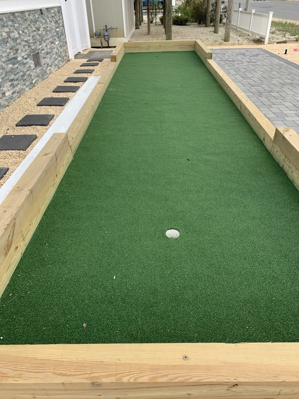 A rectangular artificial turf area with a white circular object in the center, surrounded by wooden borders and stone patterns.