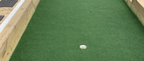 A rectangular artificial turf area with a white circular object in the center, surrounded by wooden borders and stone patterns.