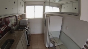 Eine kompakte Küche mit Spüle, Herd, Mikrowelle und Kühlschrank. Ein Fenster sorgt für natürliches Licht und ein kleiner Tisch bietet Platz für Sitzgelegenheiten.
