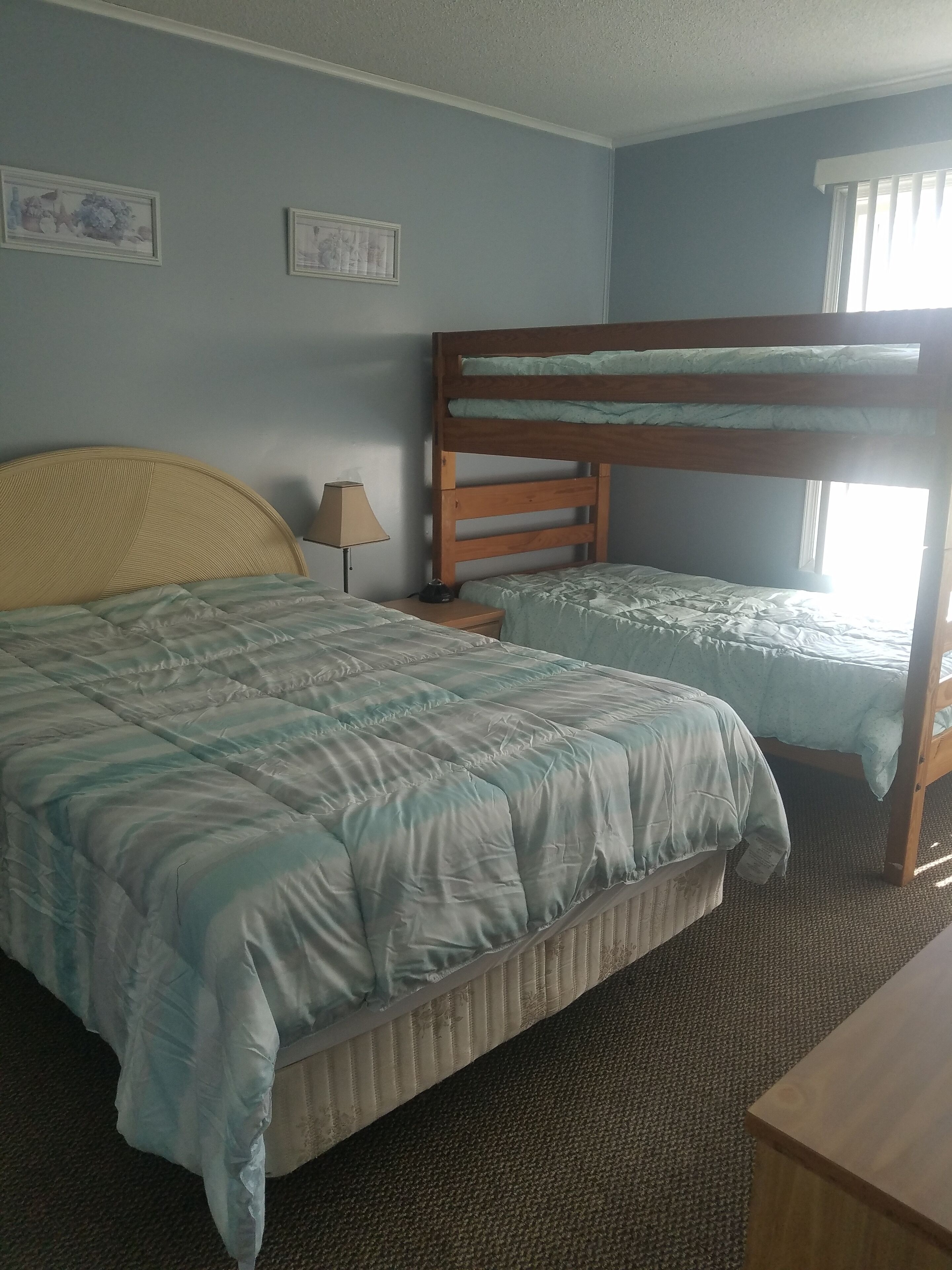 Ein Zimmer mit einem Etagenbett, einem Einzelbett, einer Lampe und einem gerahmten Bild an der Wand.