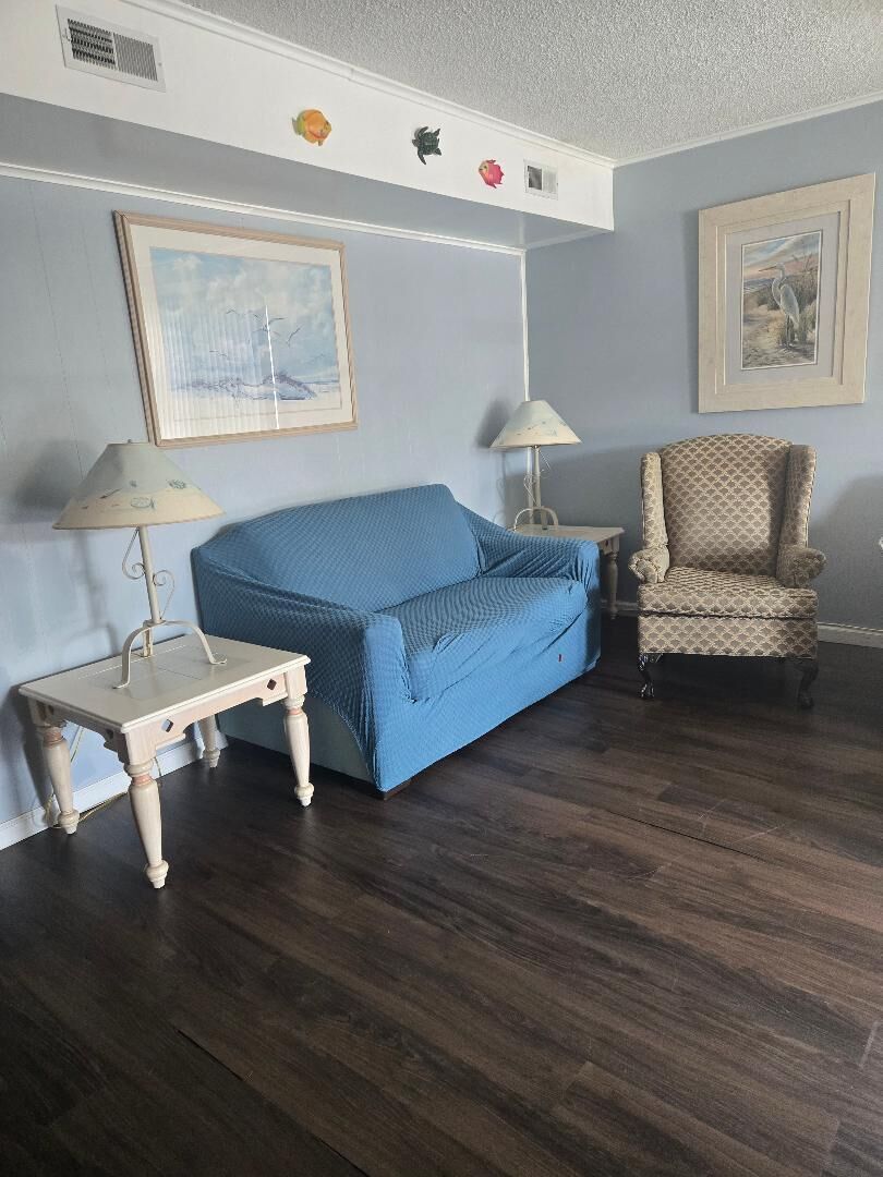 A room with a blue sofa, two lamps, a patterned armchair, and two framed pictures on the wall.