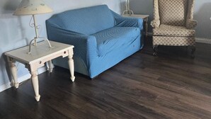 Une pièce avec un canapé bleu, deux lampes, un fauteuil à motifs et deux tableaux encadrés accrochés au mur.