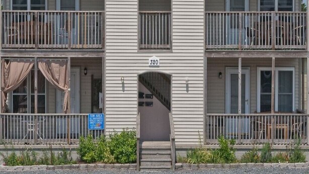 Un immeuble de deux étages portant le numéro 320, avec un balcon au deuxième étage et un escalier menant à l’entrée.
