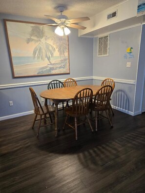 A dining area with a round wooden table and six chairs, a ceiling fan, and a beach-themed painting on the wall. - Great Location for your vacation.  Very Pet Friendly!. Close to Boardwalk/Beach. (Ocean City)