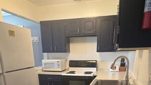 Une cuisine de taille réduite, équipée d’un réfrigérateur, d’un four à micro-ondes, d’une cuisinière, d’un évier et de meubles de rangement de couleur sombre.