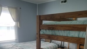 Une chambre avec deux lits superposés, une fenêtre avec des rideaux et une table de chevet avec une lampe.
