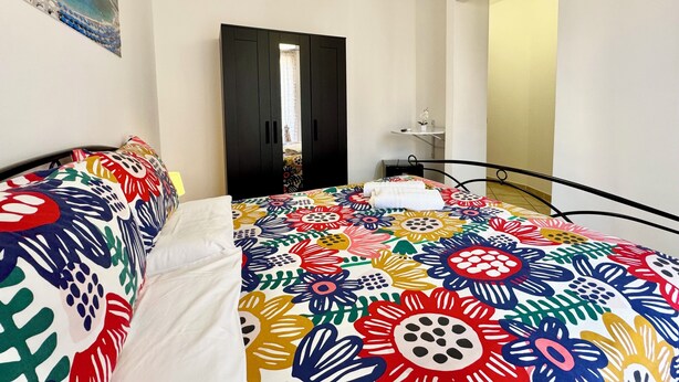 A bedroom with a bed, a nightstand, a small table, and a door.