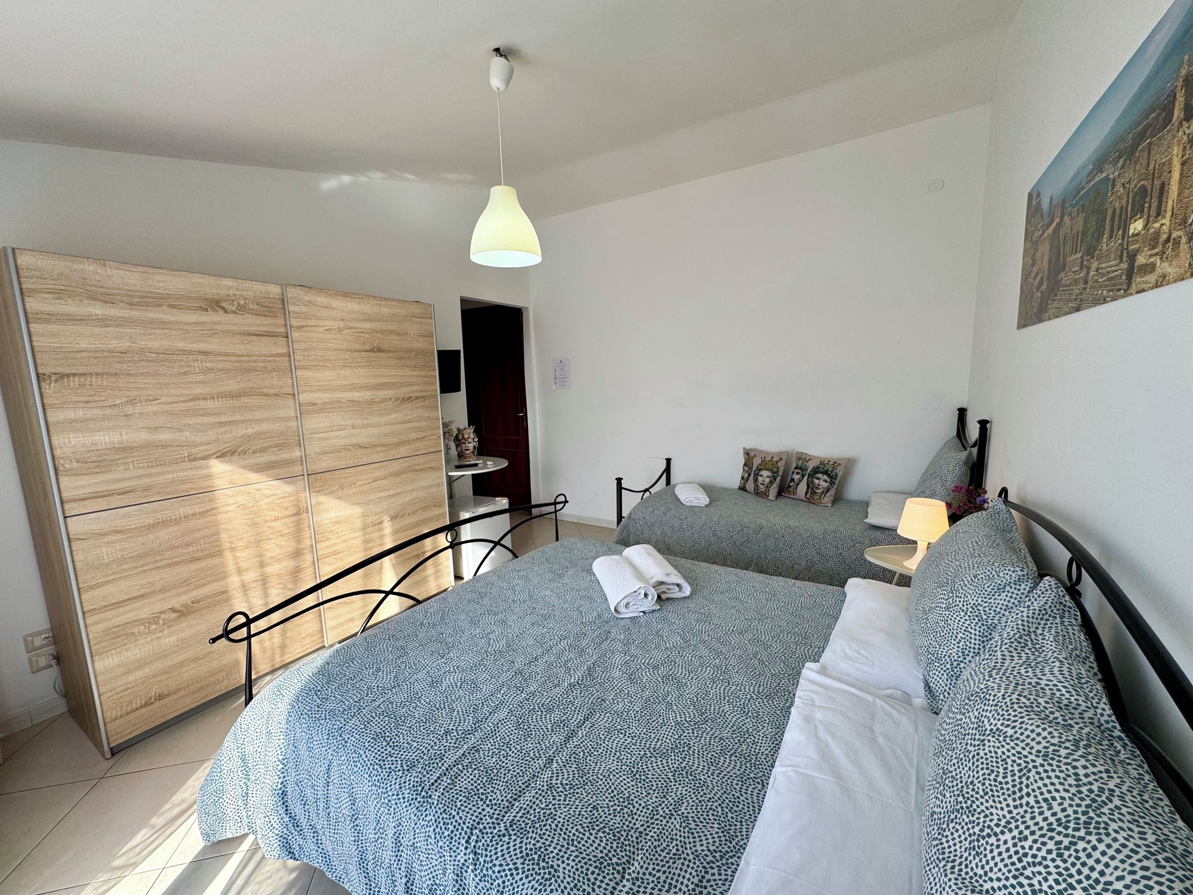 Un dormitorio con dos camas, un armario, un escritorio y una lámpara colgante.
