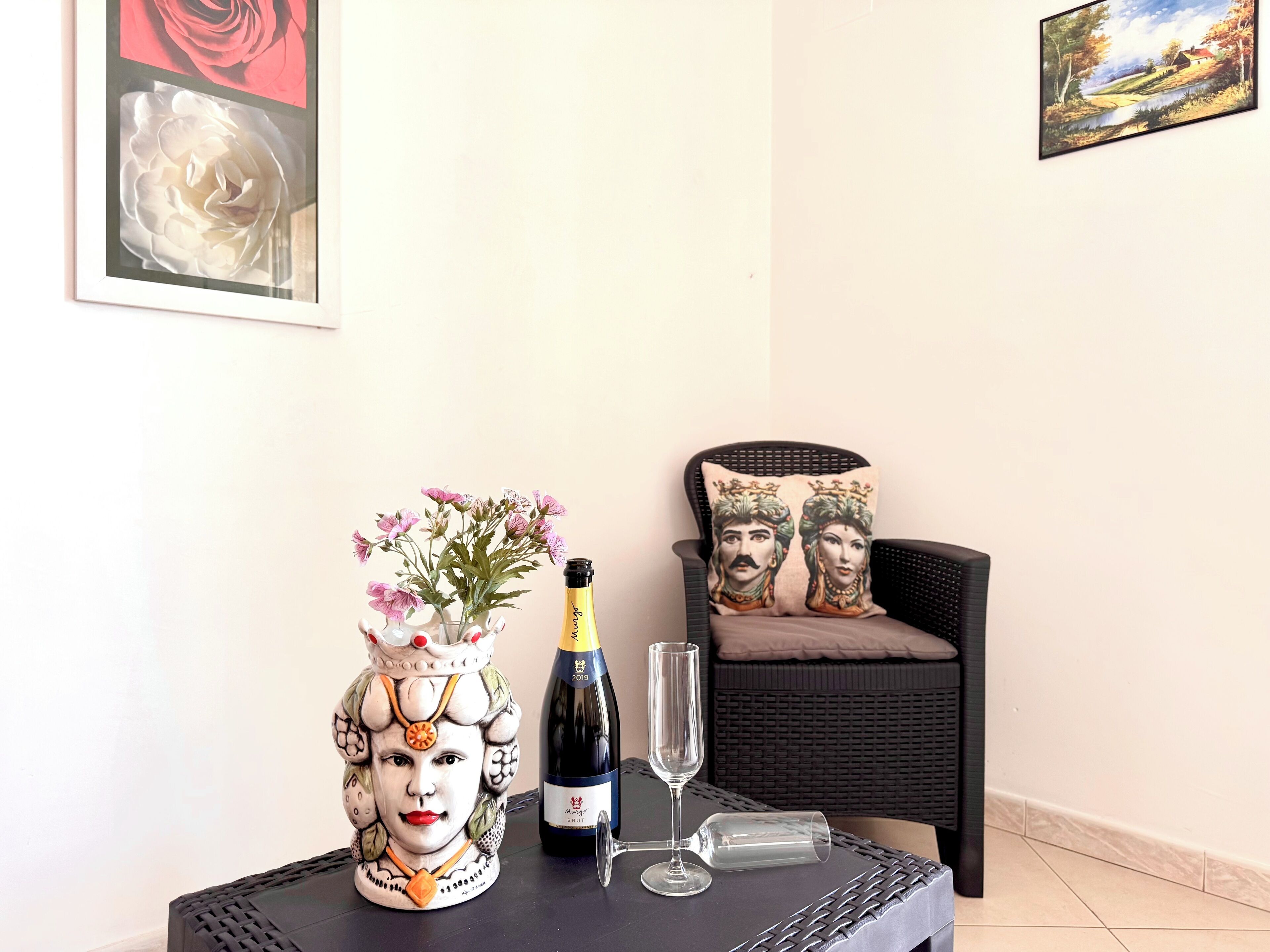 A table with a decorative ceramic pitcher, a bottle of wine, and a wine glass.