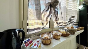 Un buffet de petit-déjeuner avec des paniers de pain et de viennoiseries, une machine à café et une fenêtre ornée de rideaux à rayures.