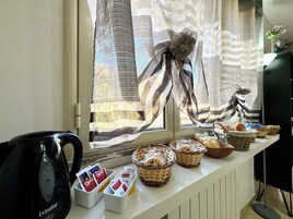Montaje de un bufé de desayuno con panes y pasteles en cestas, una cafetera y una ventana con cortinas a rayas.