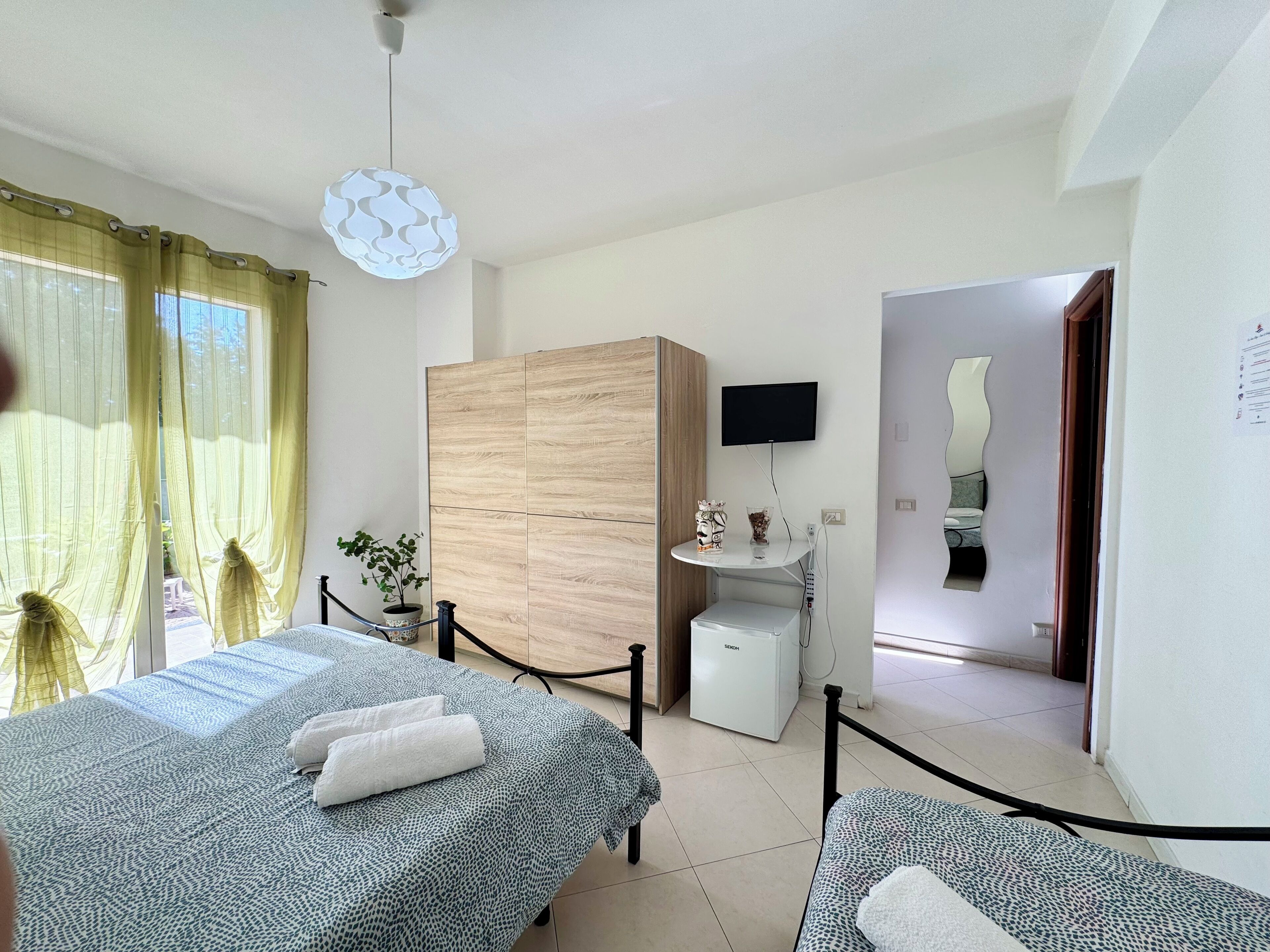 Habitación de hotel con dos camas, un armario de madera, una mesita con televisor y una planta en maceta.