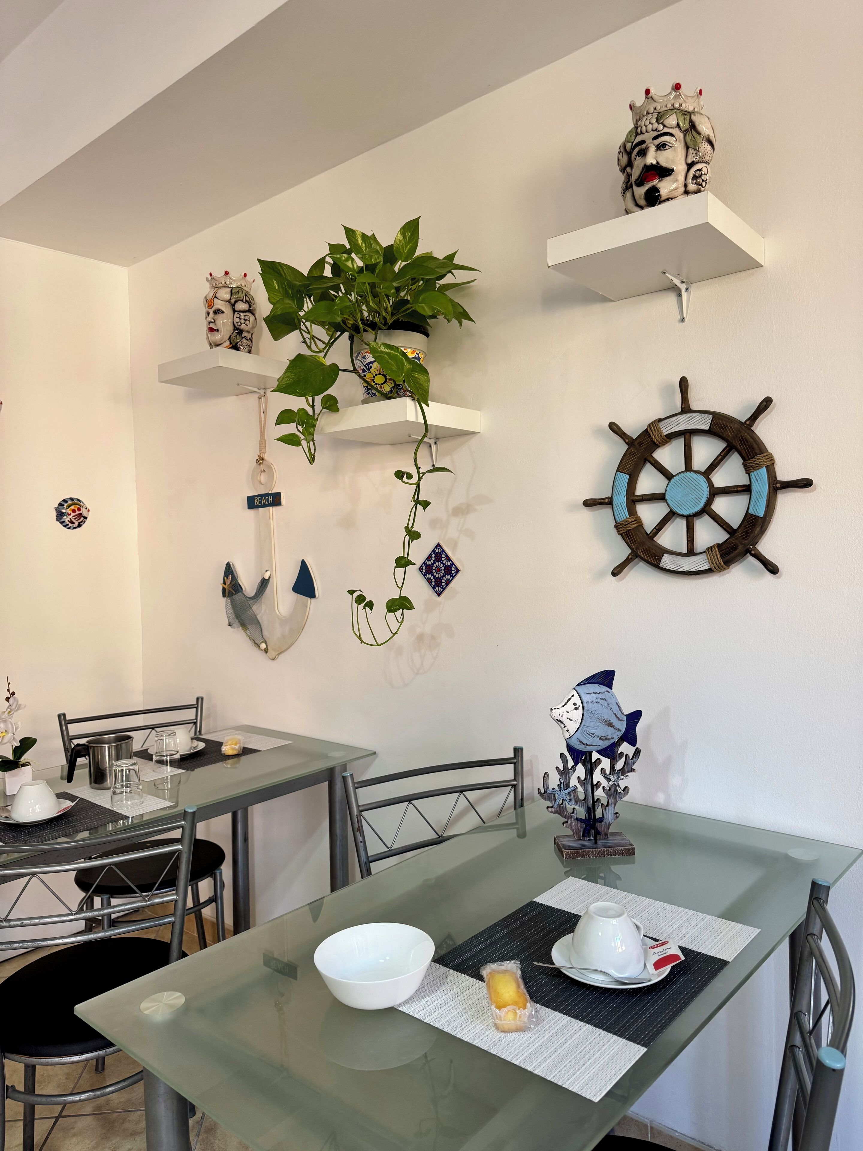 Un comedor con una mesa de vidrio, sillas y una planta decorativa colgando del techo.
