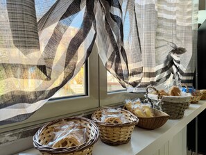 Una encimera de cocina con cestas de mimbre llenas de pan, una ventana con cortinas a rayas y vistas a árboles desde afuera.