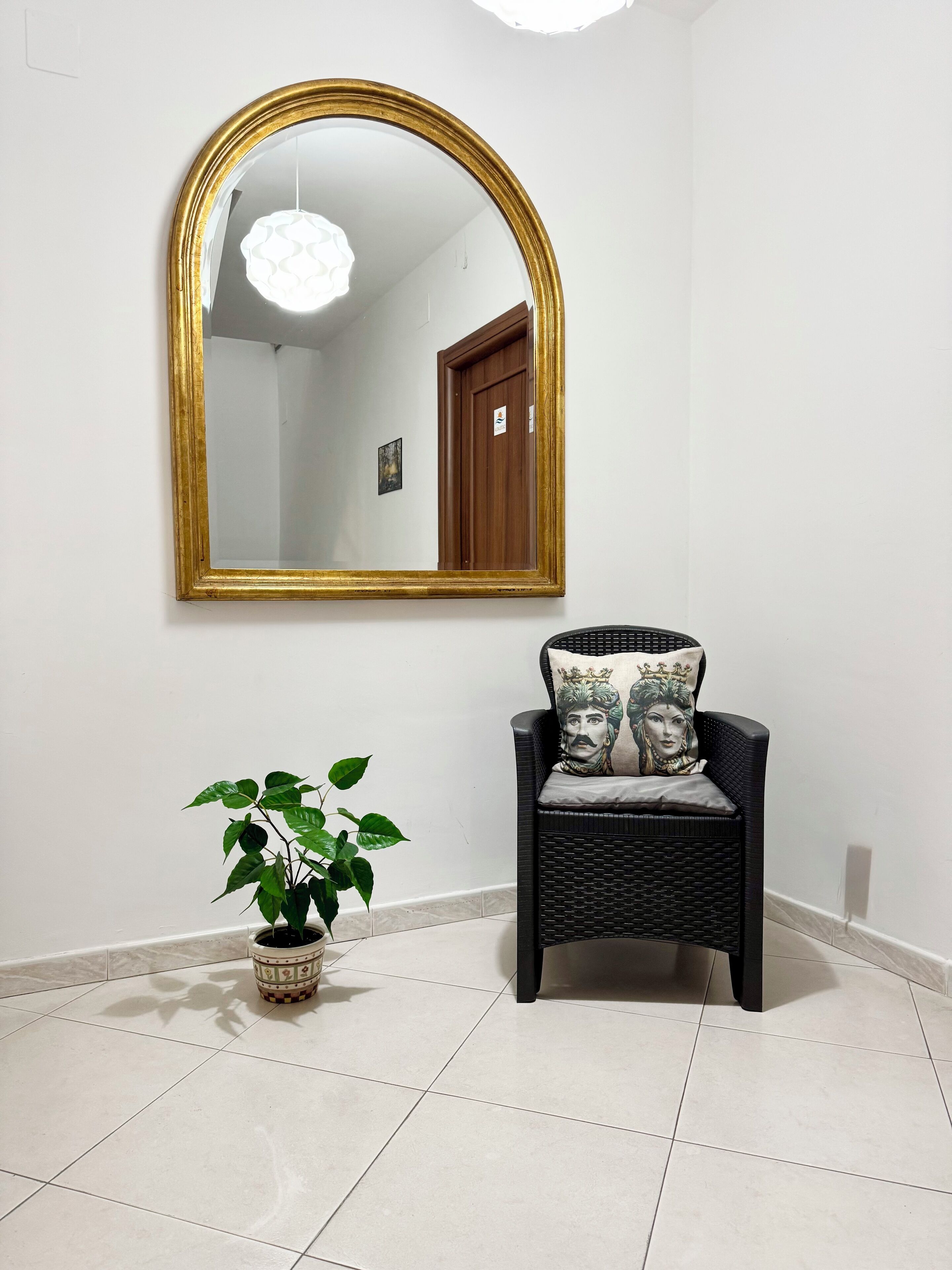 Una habitación con un espejo grande, una silla con cojines decorativos y una planta en maceta.