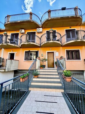Un edificio de varios pisos con balcones, una escalera central y plantas en macetas.