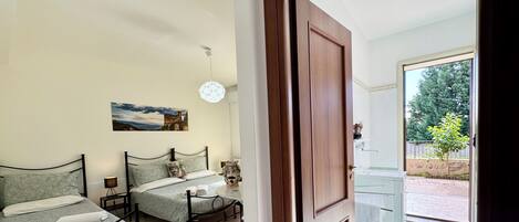 A bedroom with two beds, a painting on the wall, and a view of the outside through an open door.