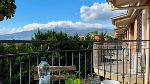 Une table de balcon agrémentée de tasses blanches, d’une bouteille d’eau et d’une petite plante, offrant une vue sur un paysage montagneux.
