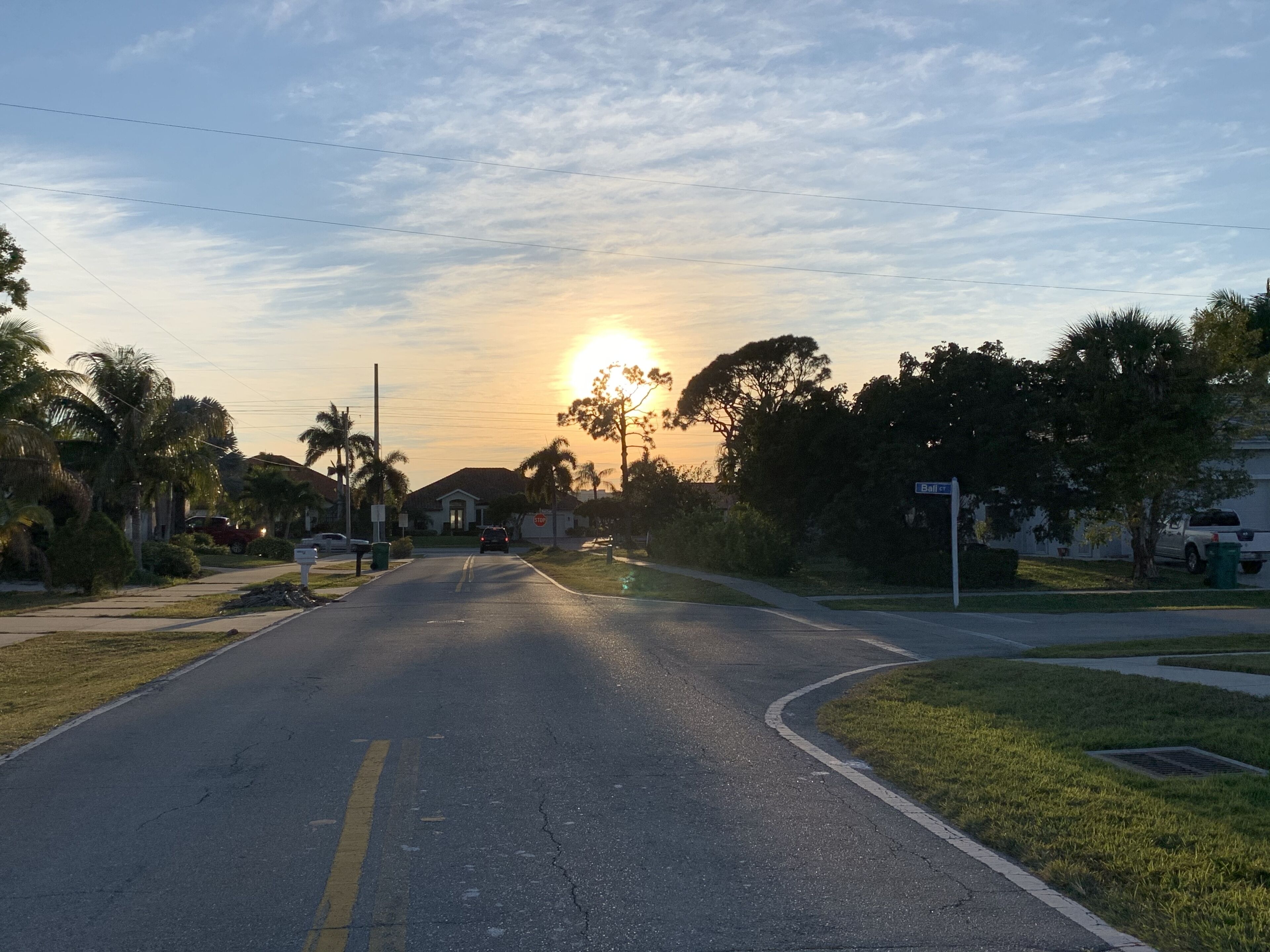 Une rue résidentielle bordée de maisons des deux côtés, un ciel dégagé et le soleil qui se couche à l’horizon.