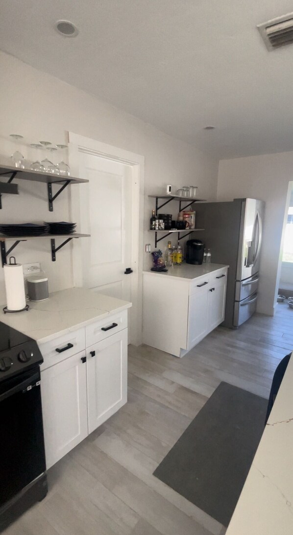 Une cuisine de taille réduite avec des meubles blancs, une cuisinière noire et un réfrigérateur encastré.
