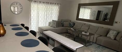 A modern living room with a dining area, a sofa set, a coffee table, and a large mirror on the wall.