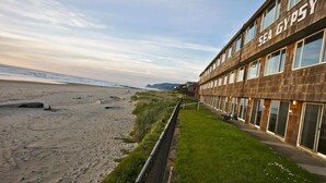 A building with the name "SEA GYPSY" on its facade, located adjacent to a beach with a grassy area and a fence in the foreground.