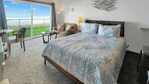 Habitación de hotel con una cama grande, un sofá, una mesa de comedor y vista al océano.