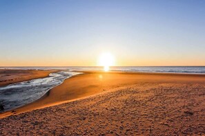 Ein Strand mit Sonnenuntergang, sandigem Ufer und Fußabdrücken.