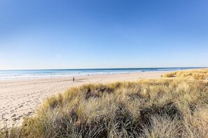 Ein Strand mit Sand und Gras im Vordergrund und dem Meer im Hintergrund.