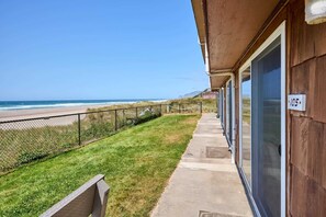 Une propriété située en bord de mer, avec un chemin en béton menant à un bâtiment en bois doté de grandes fenêtres.