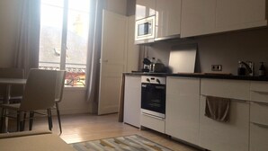 A compact kitchen with a microwave, oven, and a small countertop. There's a dining area with a chair and a table. - Charming two-room refurbished 50m from the sea (Houlgate)