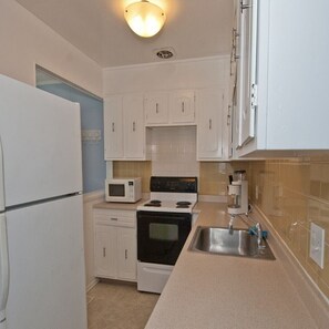 A compact kitchen with white cabinets, a microwave, a stove, and a sink.