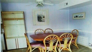Un comedor con una mesa y sillas de madera, un ventilador de techo y dos cuadros en la pared.