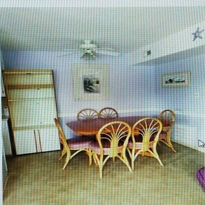 A dining area with a wooden table and chairs, a ceiling fan, and two framed pictures on the wall.