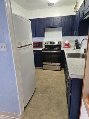 Cocina con gabinetes azul oscuro, estufa de acero inoxidable, refrigerador blanco y encimera de mármol.